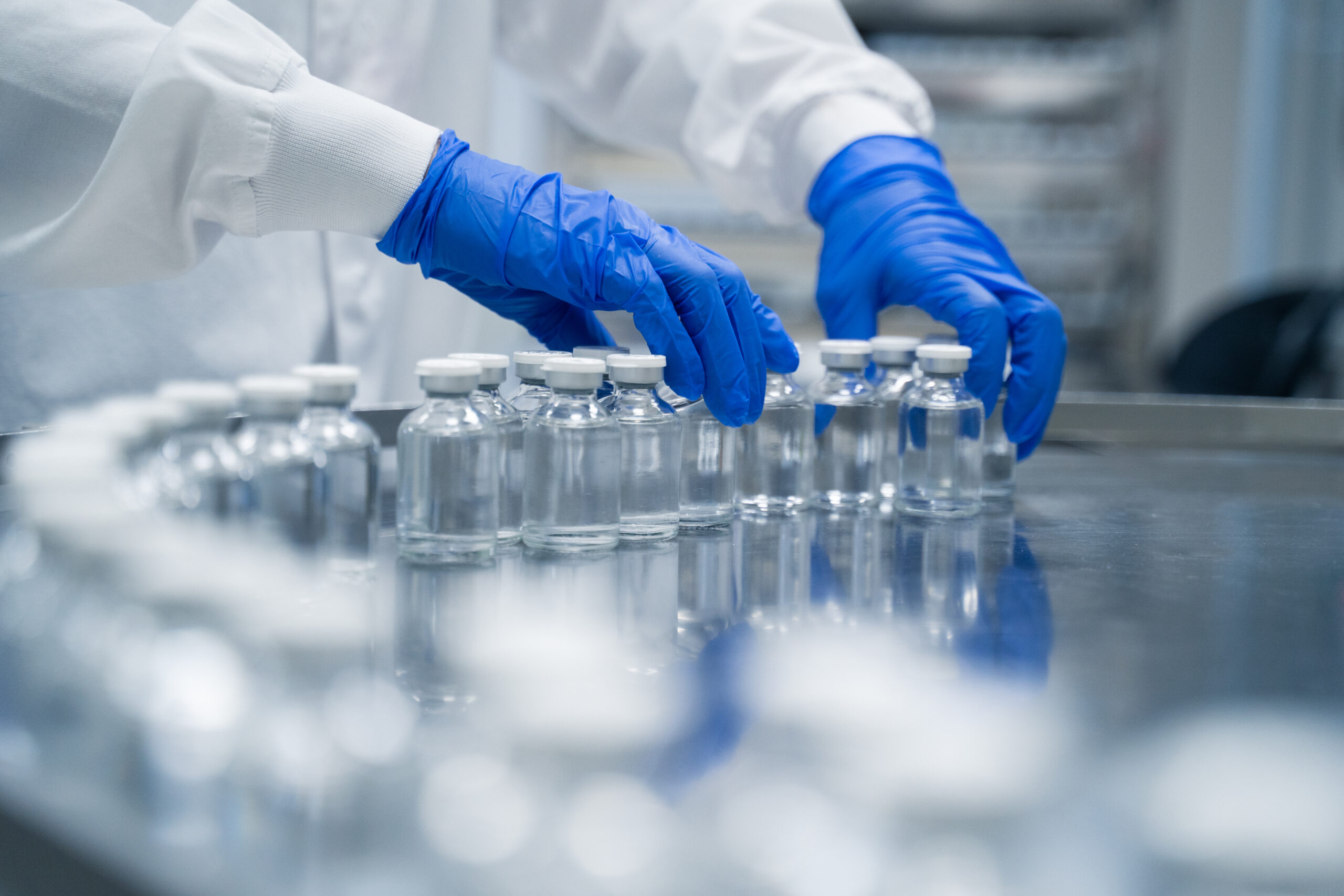 Detail of hands working in pharmaceutical factory manufacturing sterile bottles
